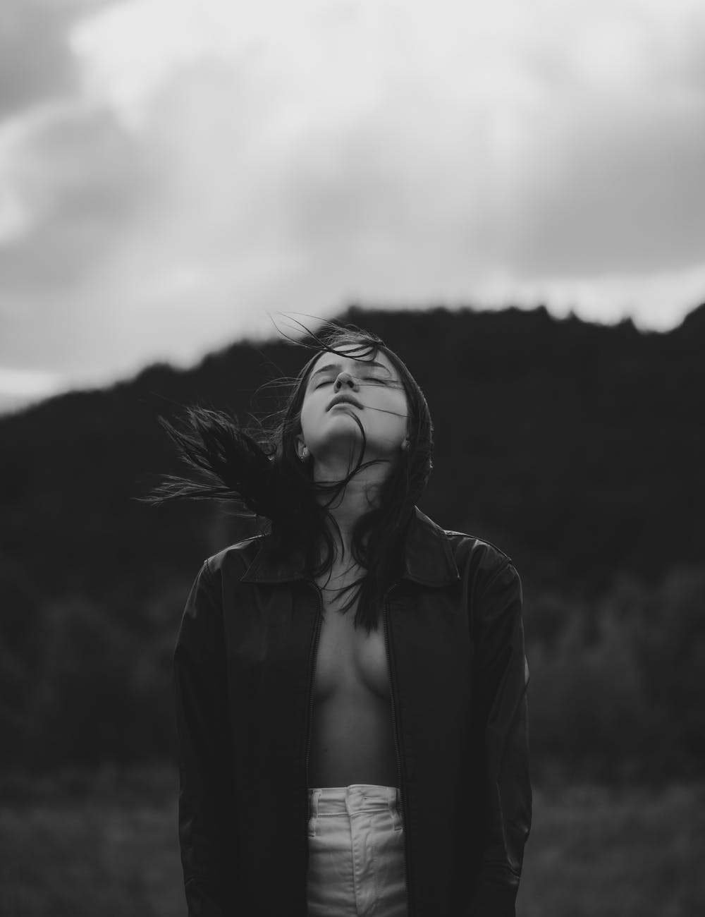 thoughtful young woman standing in wind with closed eyes under overcast sky
